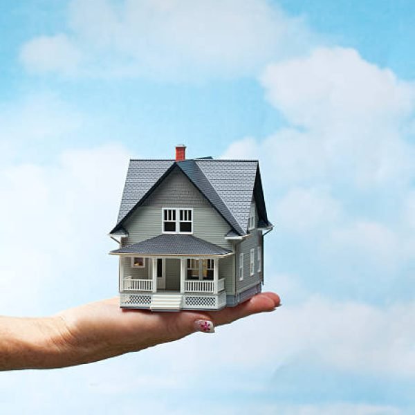 Woman holding model house with clouds.